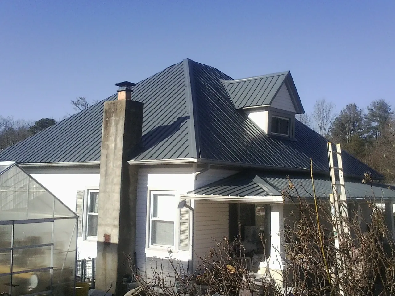 Dark blue standing seam metal roof on a white farmhouse with dormer — Slate & Tile Roof Repair by Roofing Brothers in Mcmechen