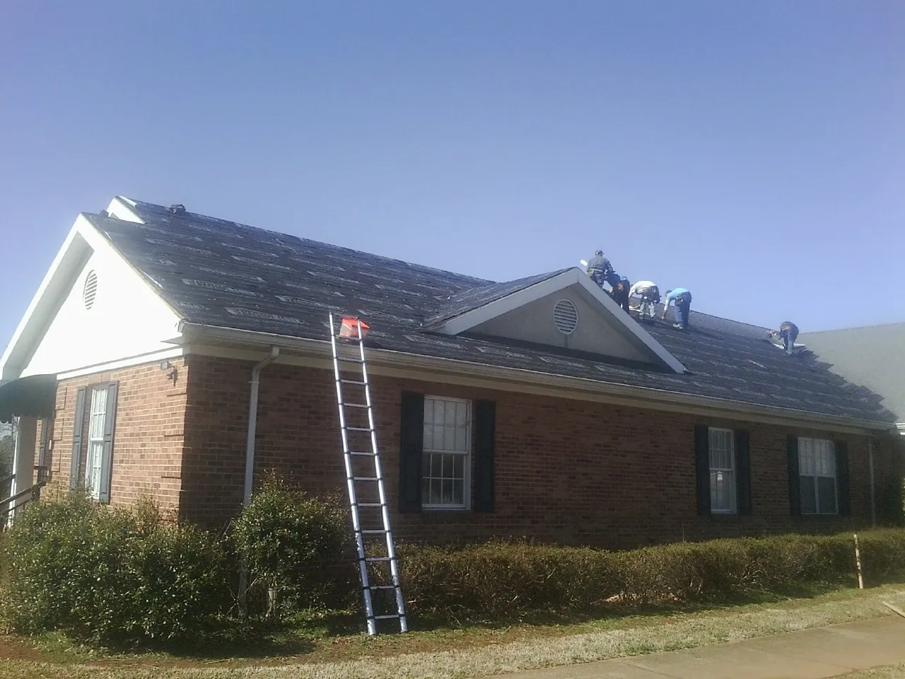 Crew tearing shingles off a brick ranch roof with a ladder set — Emergency Roof Repair work by our crew in Mcmechen