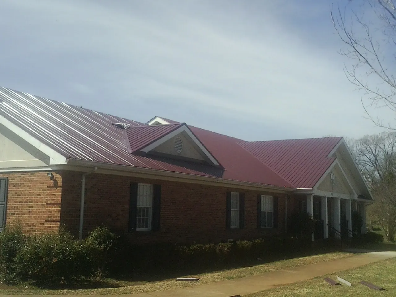 Red metal roof with gabled entries on a long brick building, from a Hail Damage Roof Repair job in Mcmechen