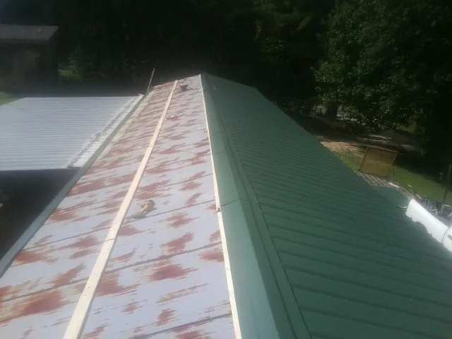 Old rusted panels beside newly installed green metal roofing — Wind Damage Roof Repair by Roofing Brothers in Mcmechen