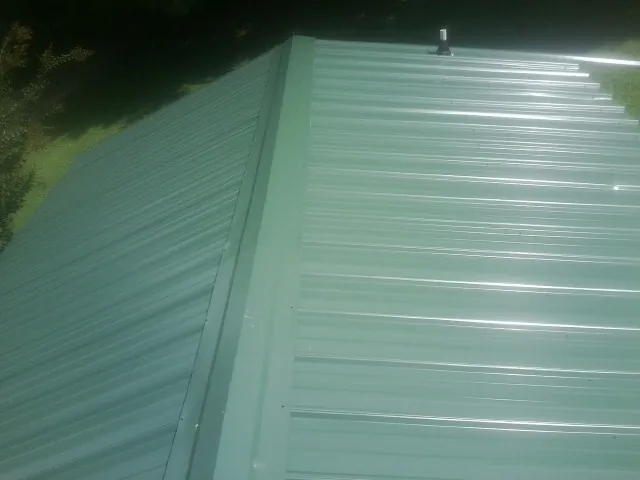New green metal panels meeting at the ridge of a roof — Flat Roof Repair work by our crew in Mcmechen