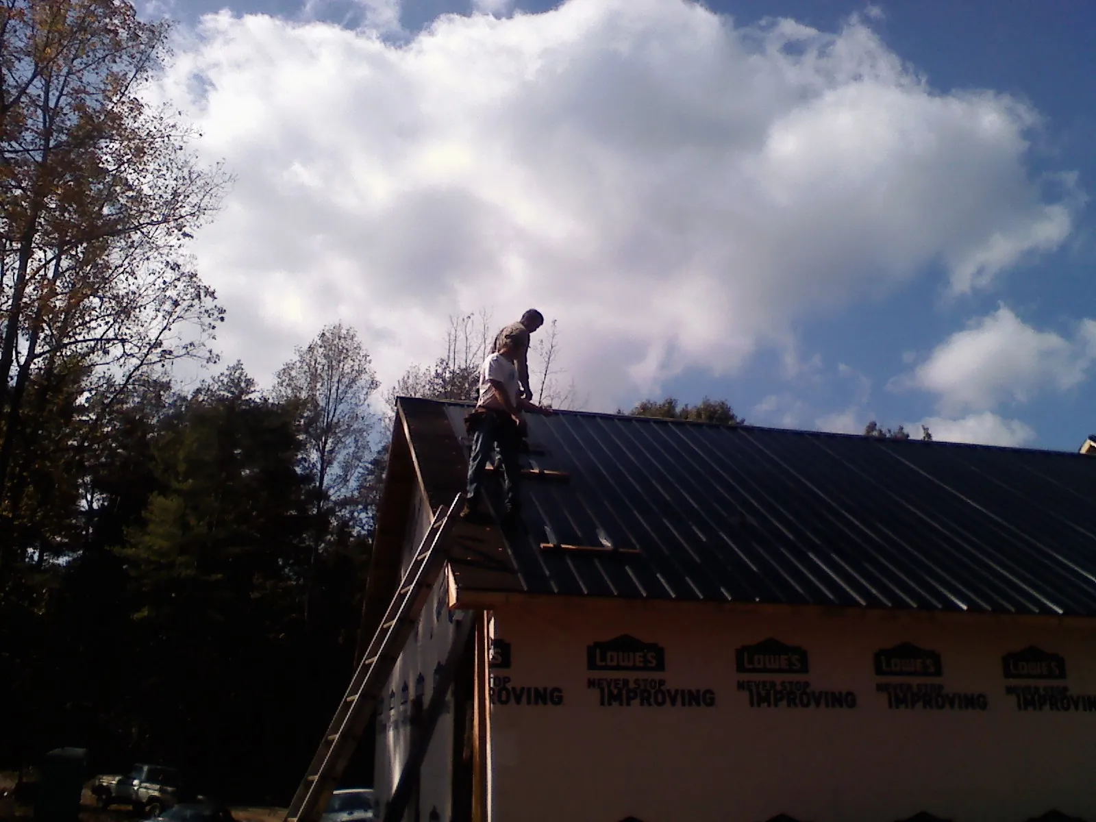 Roofer fastening dark metal panels high against a cloudy sky, from a Roof Inspection job in Mcmechen